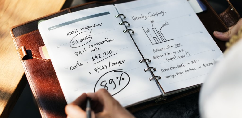 A conference folder laying open, with campaign planning number and graphs being written onto 2 pages visible in the ring binders.