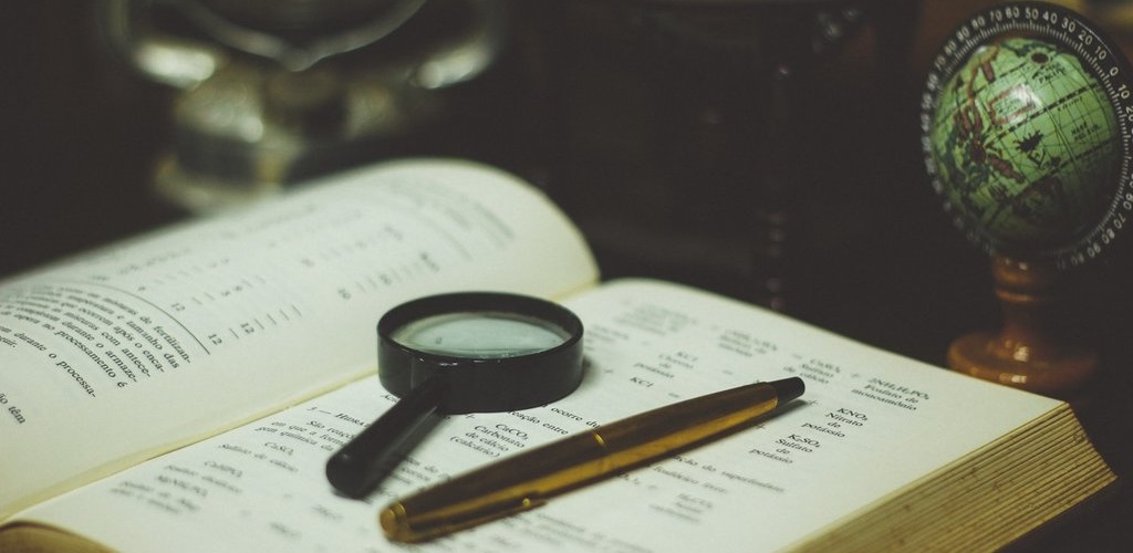 A book lies open, with a magnifying glass and pen on the right hand page. A small globe sits next to it.