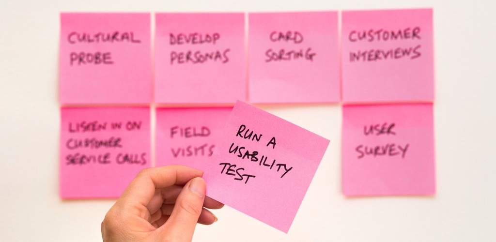 8 user experience Post-Its on a wall, one is being held up to the camera that reads 'Run a Usability Test'